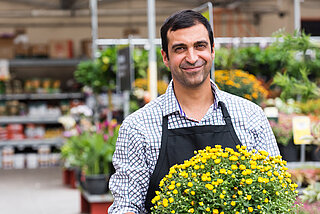 Lächelnder reifer männlicher Florist, der im Gartencenter posiert und einen Topf mit Blumen hält